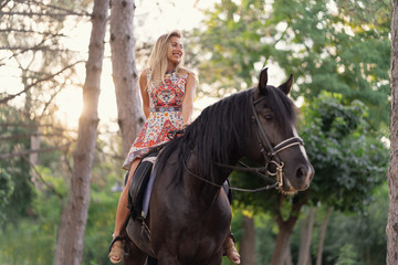 Obraz premium Young woman in a bright colorful dress riding a black horse