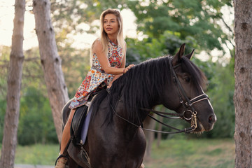 Obraz premium Young woman in a bright colorful dress riding a black horse