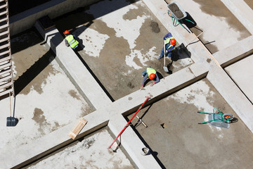 Uniformed workers clean sand on a construction site, top view.