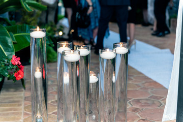 Various heights of water tubes hold outdoor floating candle decorations for the party all have glowing flames on the wicks.