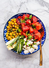 Colorful turmeric chickpea watermelon salad with feta cheese, tomatoes, zucchini, mint and balsamic vinegar on marble table. Summer fresh easy lunch. Flat lay