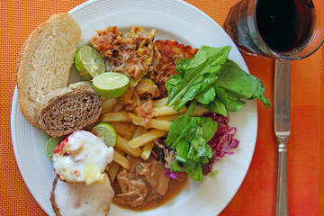 Portion of french fries with piece of meat leaves of lettuce, cabbage and lime