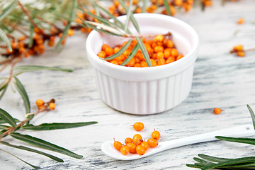 Natural, organic sea buckthorn berry in bowl and a on white wooden background. Branch of sea...