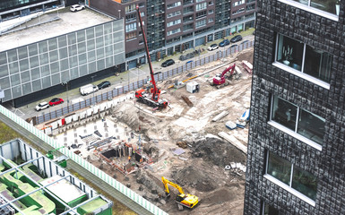 A red crane in a construction work area with pile sand surrounded of others buildings. 