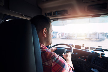 Professional middle aged truck driver in casual clothes driving truck vehicle going for a long transportation route delivering goods to the market. Transportation services.