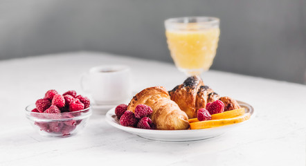 Breakfast with croissants, a cup of coffee, raspberries and orange juice