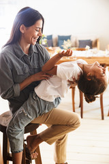 Image of attractive family woman smiling and having fun with her little daughter at cozy apartment