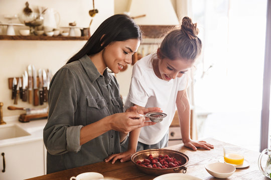 Image of happy family woman and her little daughter cooking together meal with raspberry at cozy apartment