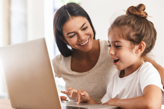Image of joyful family woman and her little daughter smiling and using laptop computer together in apartment