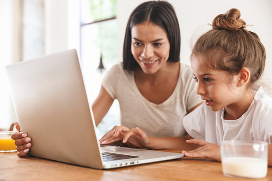 Image of happy family woman and her little daughter smiling and using laptop computer in apartment