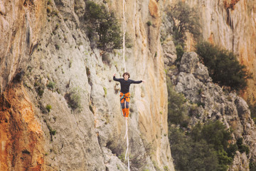 A man is walking along a stretched sling. Highline in the mountains. Man catches balance....