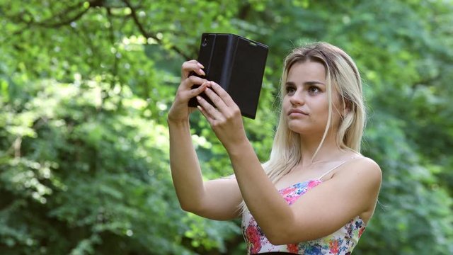 Beautiful blonde girl taking photos for Social Media in a park while smiling and being happy.