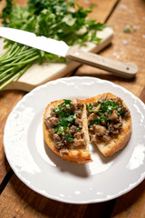 Toasts with mushrooms on white plate on wooden kitchen table