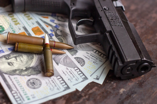 Black gun and weapon bullets on American dollars background. Military industry, war, global arms trade and crime concept.