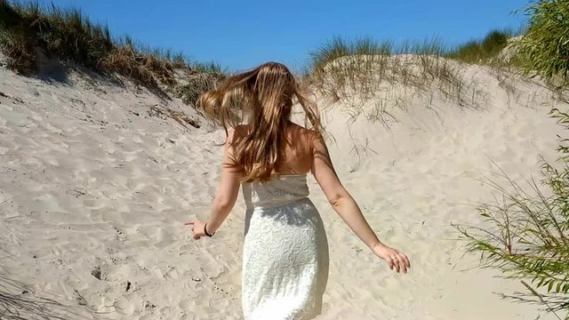 Following a beautiful woman running through sand dunes in the sun on Liepaja beach in Latvia