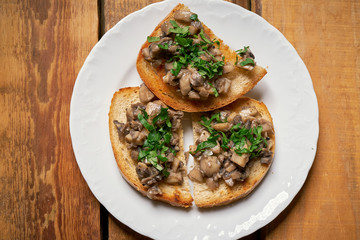 Toasts with mushrooms on white plate on wooden kitchen table