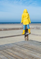 Frau in gelbem Regenmantel guckt aufs Meer 