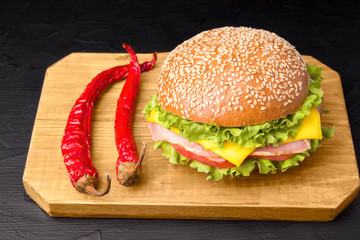 Bun with ham, cheese, herbs and tomato. Red pepper next to the board. Sandwich. Dinner. Fast food