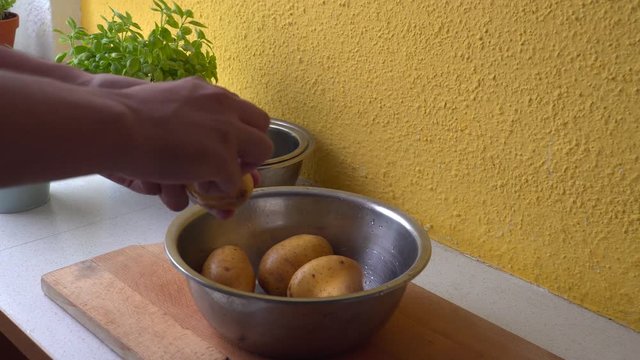 Male hands picking potato from silver boal and peeling it with a peeler medium shot with plants in background