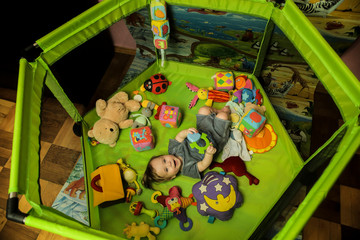 baby boy lies in a green playpen, there are a lot of toys around - teddy bear, cubes, rattles, soft toys © ShU studio