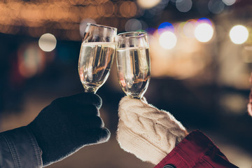 Close-up cropped view of two hands wearing warm outfit holding in hands glasses sparkling wine...