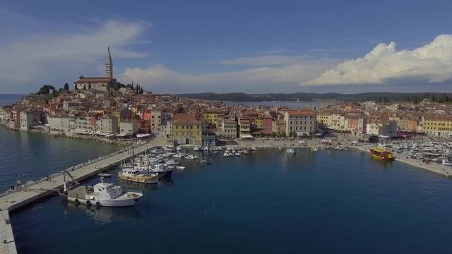 Aerial drone push in shot to Rovini over the harbour, to the old historic city, as tourists walking by on a sunny summer day.