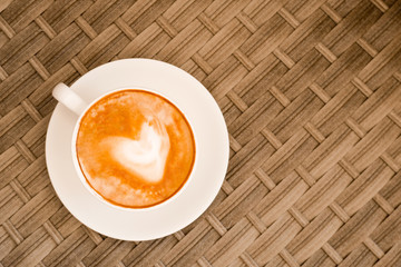 Heart made of cappuccino foam in white cup on wood table at cafe. Top view. Place for text. Bewerages, coffee lovers and morning menu concept. Stylish toning.