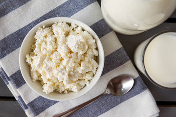 plate of natural cottage cheese, a glass of cow's milk,  bottle of milk, spoon,  striped towel on a gray background