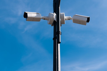 Two white surveillance cameras on the metal lamp post against blue sky. Security of the whole territory. Security service is watching. Copy space.