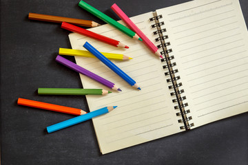 Back to school. Colored pencils and notebook on chalkboard