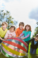 Group of kids rolls a ball over a meadow