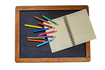 Back to school. Colored pencils and notebook on chalkboard