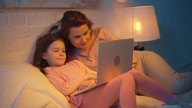 mother and daughter watching movie on laptop in bed at night