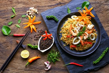 Flat lay of instant noodles with stir fried spicy seafood and various herbs and spices on black...