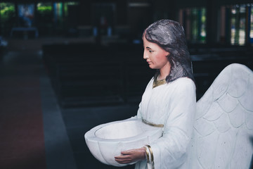 Angel statue holding bowl of holy water at the Church's entrance. Selective focus. Copy space.