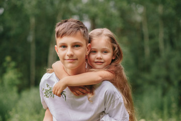 brother holds sister on shoulders outdoors in summer