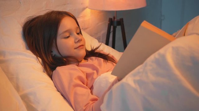 child lying in bed and reading book at night