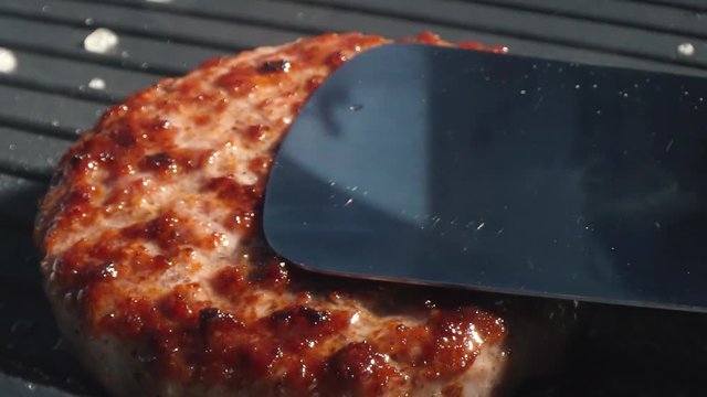 Close-up big beef cutlet is grilled, the chef presses the cutlet with an iron spatula to the grill. Slow motion video