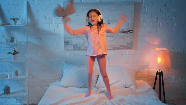 child in headphones jumping on bed at night