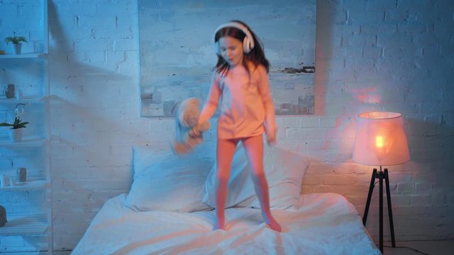 excited child in headphones dancing on bed at night