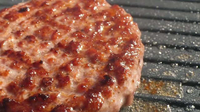 Close-up big beef cutlet is grilled, the chef presses the cutlet with an iron spatula to the grill. Slow motion video