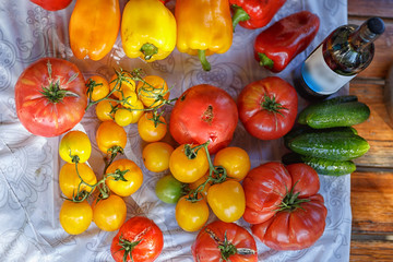 tomatoes, cucumbers and sweet peppers on a transparent oilcloth on a wooden table
