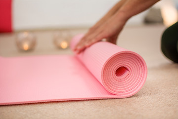 Woman hands winding the pink yoga mat. Copyspace on the left side.