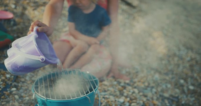Young mother with toddler putting out barbecue on beach