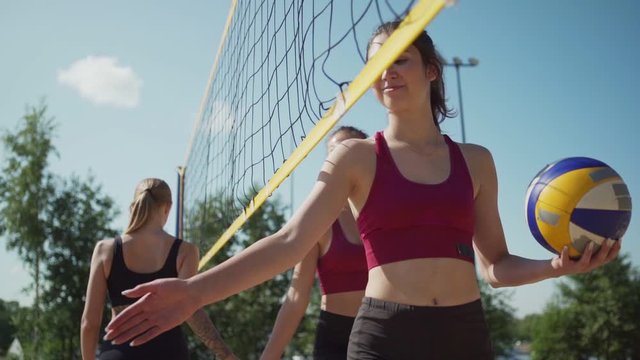Two teams of female beach volleyball players walking at opposite sides of net in slow motion and giving low fives. Athletes greeting each other before match or thanking after game