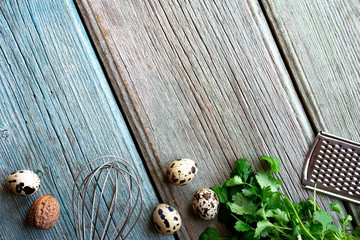 Quail eggs, whisk, grater and parsley on a blue and grey wooden table top view. Cooking, food background, copy space.