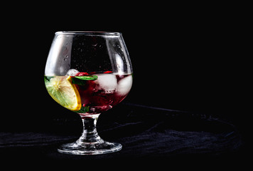 Cocktail with ice lemon mint strawberries in a cognac glass on a black background