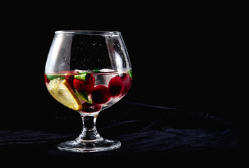 One cocktail with ice lemon mint strawberries cherries in a cognac glass on a black background