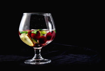 One cocktail with ice lemon mint strawberries sweet kiwi in cognac glass on a black background one