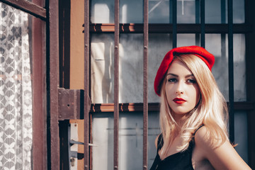friendly confident beautiful young woman wearing a red beret on her long blond hair in town in summer sunshine